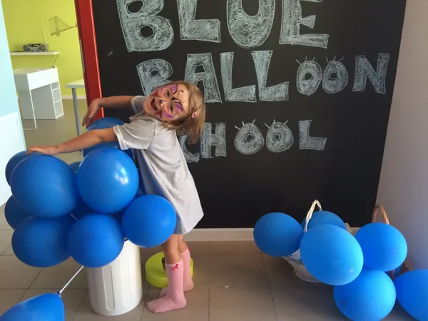 Dziewczynka pozuje przy niebieskich balonach i tablicy Welcome to Blue Balloon School