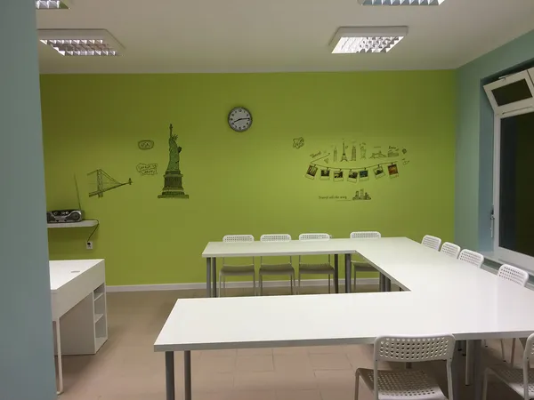 Sala lekcyjna z zieloną ścianą, białymi stolikami i dekoracją London Bridge