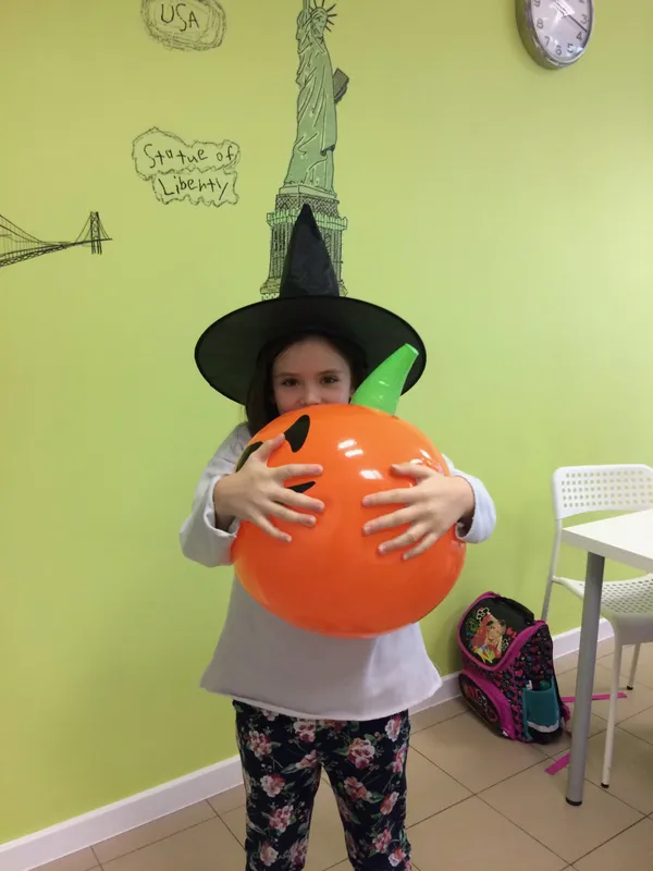 Dziewczynka w stroju czarownicy trzyma pomarańczowy balon podczas Halloween w szkole