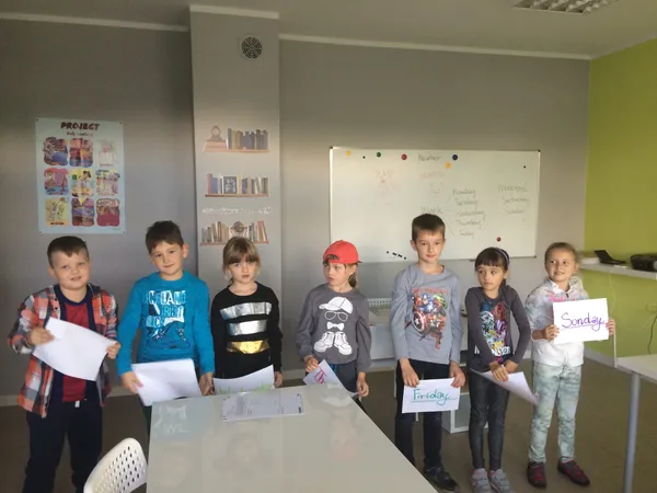 Dzieci stoją w rzędzie w sali lekcyjnej i trzymają prace w rękach